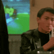 a man in a black jacket is sitting at a table with a cell phone in his hand ..