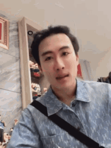 a man wearing a denim shirt with a black strap around his shoulder looks at the camera .