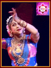 a woman in a blue and red outfit is dancing in front of a sign that says ' bharatnatyam ' on it