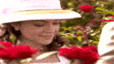 a woman wearing a white hat is smiling while smelling red roses