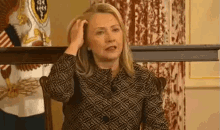 a woman scratches her head in front of a flag