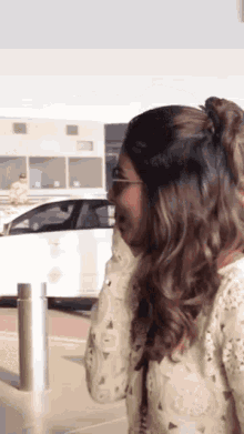 a woman standing in front of a white car talking on a cell phone
