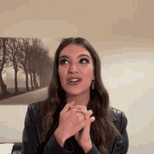a woman wearing a leather jacket and earrings is making a funny face in front of a painting of trees