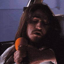 a man with long hair and a beard is holding an orange object in his hand
