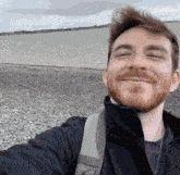 a man with a beard is smiling while taking a selfie on a beach