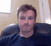 a man with a mustache is sitting in a chair and making a funny face