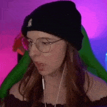 a woman wearing a black beanie and glasses is sitting in front of a pink and purple background .