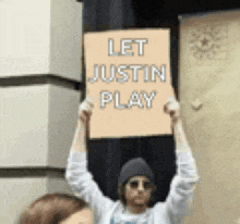 a man holding a sign that says let justin play