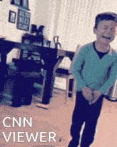 a boy in a blue sweater is standing in front of a cnn viewer
