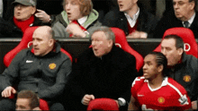 a man in a red manchester united jersey is sitting in the stands watching a soccer game