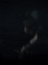 a man with long hair and a mustache is smoking a cigarette in a dark room