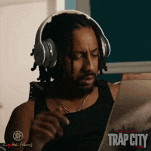 a man wearing headphones looks at a piece of paper that says trap city on it