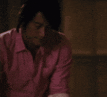 a man in a pink shirt is sitting down in a dark room