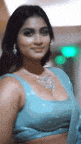 a woman wearing a blue top and a necklace is looking at the camera