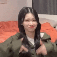 a woman in a green jacket is holding her hair and making a face .