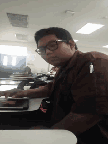 a man wearing glasses is sitting at a desk in a classroom