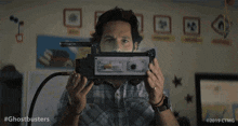 a man in a plaid shirt is holding a device in front of his face .