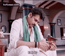a man wearing a green scarf and a white shirt is sitting on a table holding a sword .