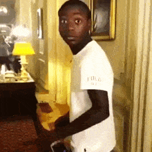 a young man wearing a white polo shirt stands in a room