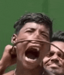 a man is screaming with his mouth open while another man is holding a wire around his neck .