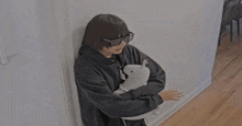 a person wearing sunglasses is holding a stuffed animal while leaning against a wall
