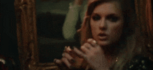 a woman is looking at herself in a mirror and applying lipstick .