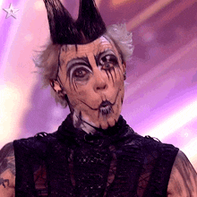 a person with a mohawk and face paint looks at the camera with a star in the background