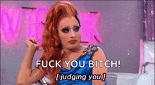 a drag queen is sitting on a couch and saying `` fuck you bitch ! judging you '' .