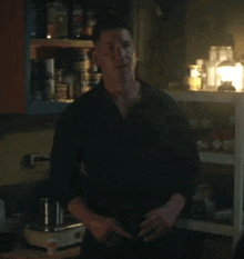 a man in a black shirt is standing in front of a shelf with jars on it