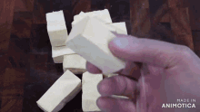 a hand is holding a piece of tofu in front of a wooden cutting board .