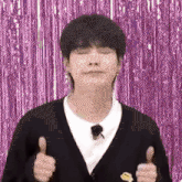 a young man is giving a thumbs up sign in front of a purple background .
