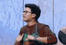 a man wearing glasses and an apron is standing in front of a wall and giving a thumbs up .