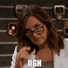 a woman wearing glasses and a white jacket is pointing at the camera with the word ugh written on her face .