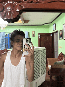 a man in a white tank top takes a picture of himself in the mirror