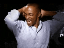 a man in a blue shirt is holding his head with his hands .
