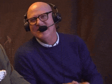 a bald man wearing glasses and headphones with a microphone is smiling .