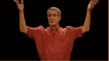 a man in a red shirt is holding his arms up in the air .