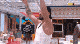 a man in a white tank top is standing in a room with his arms outstretched .