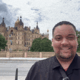 a man in a black shirt smiles in front of a large castle