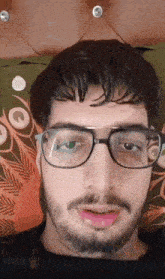 a man with glasses and a beard is sitting on a bed .
