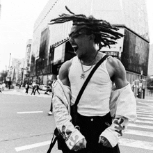 a black and white photo of a man with dreadlocks standing on a street .