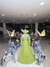 a woman in a green dress is standing in front of flowers