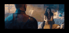 a woman is sitting on a bed talking to a man in a movie