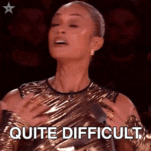 a woman in a gold dress says " quite difficult " in front of a microphone