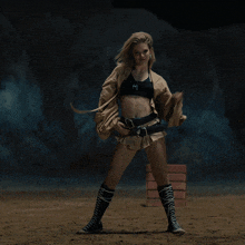 a woman in a crop top and shorts is standing on a dirt field