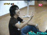 a young man is sitting on the floor in front of a fan and the words super ng are on the wall behind him