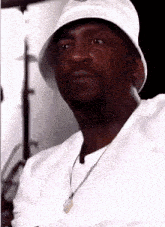 a man wearing a white hat and a necklace looks at the camera