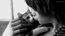 a black and white photo of a woman kissing a cat on the cheek .