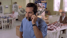 a man in a blue scrub top is talking on a cell phone in a room .