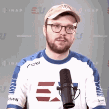 a man wearing glasses and a hat stands in front of a microphone
